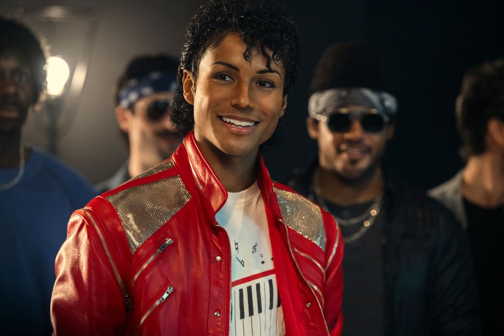 A smiling man in a red leather jacket with sequins, standing in front of other people wearing sunglasses.