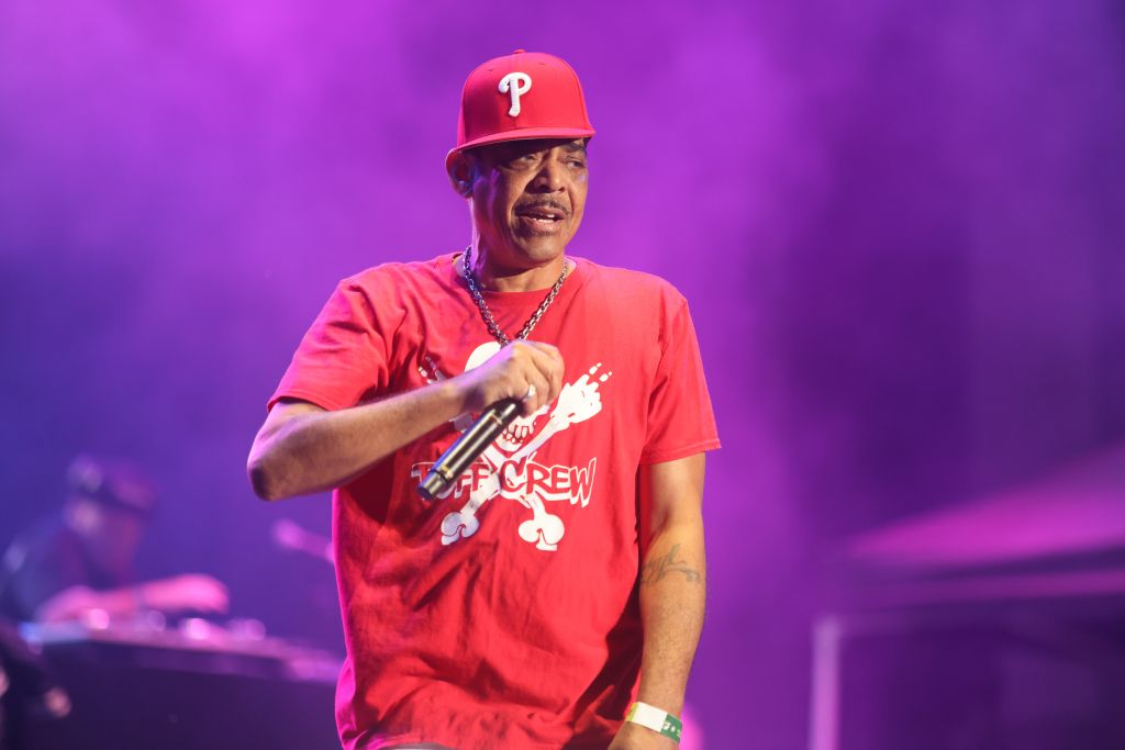 A man wearing a red Philadelphia Phillies baseball cap and shirt performing on stage with a microphone.