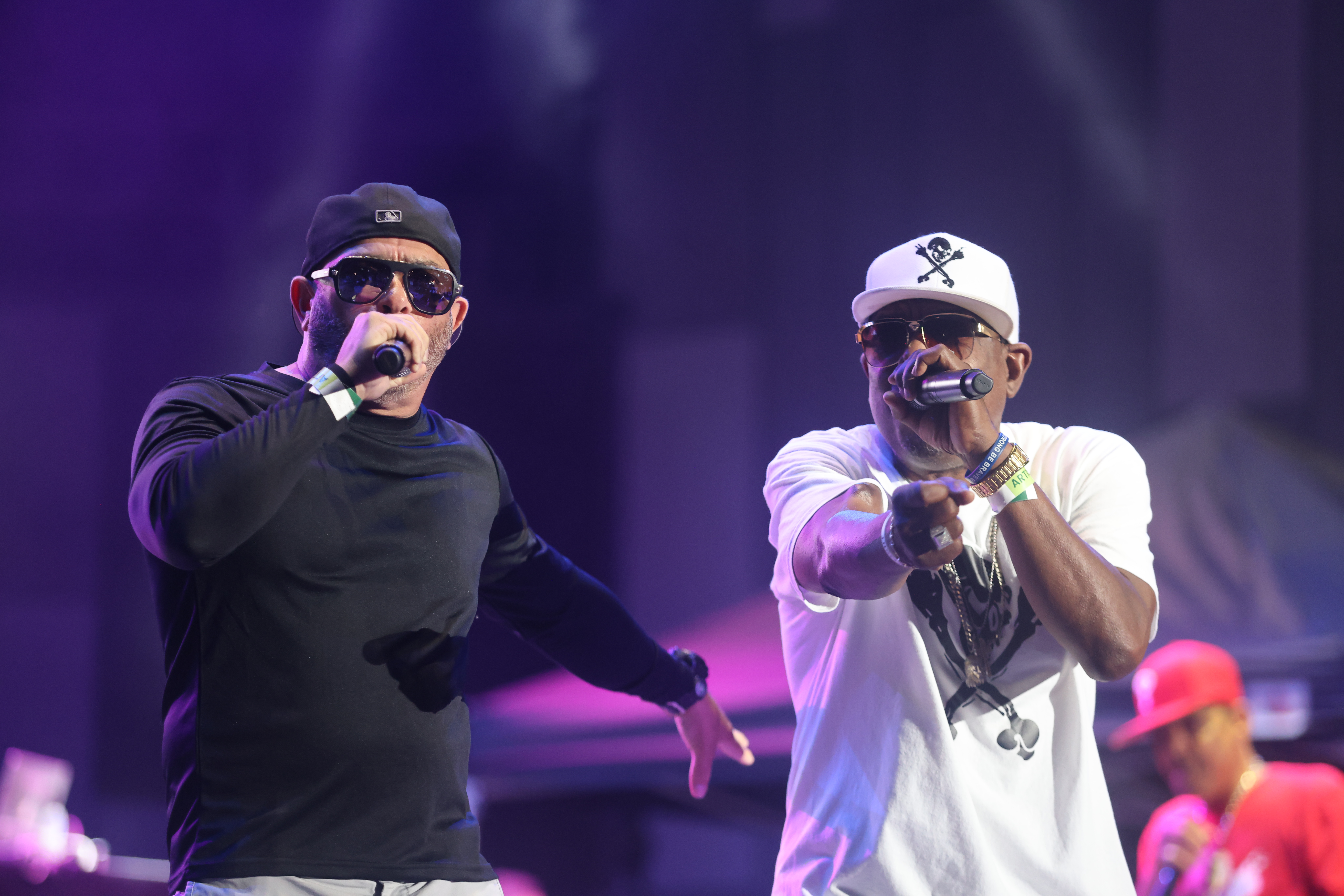 Two men performing on stage, one wearing a black hat and the other a white hat with a skull and crossbones logo.