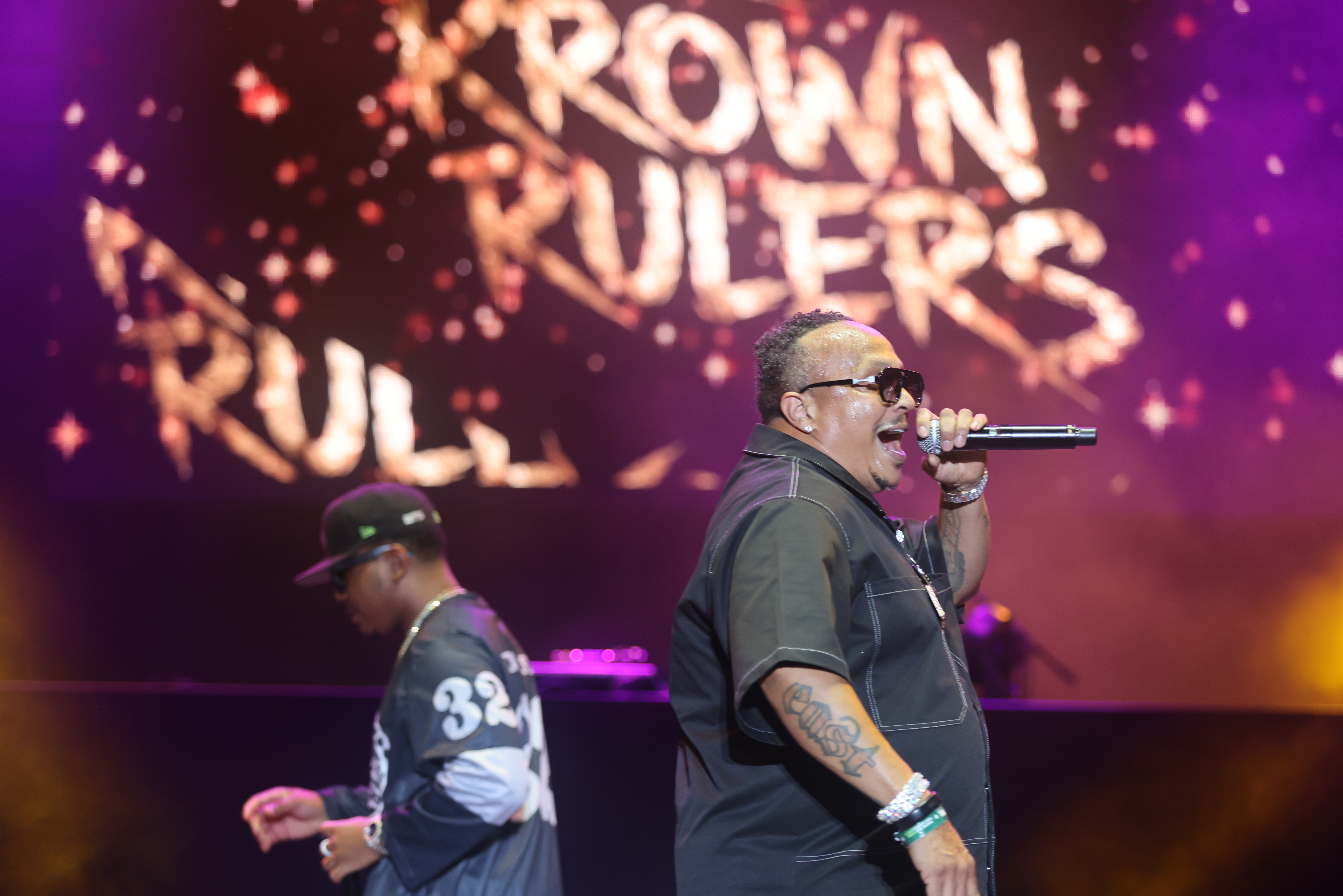 Two performers on stage, one holding a microphone and singing, with the text "Crown Rulers" displayed behind them.