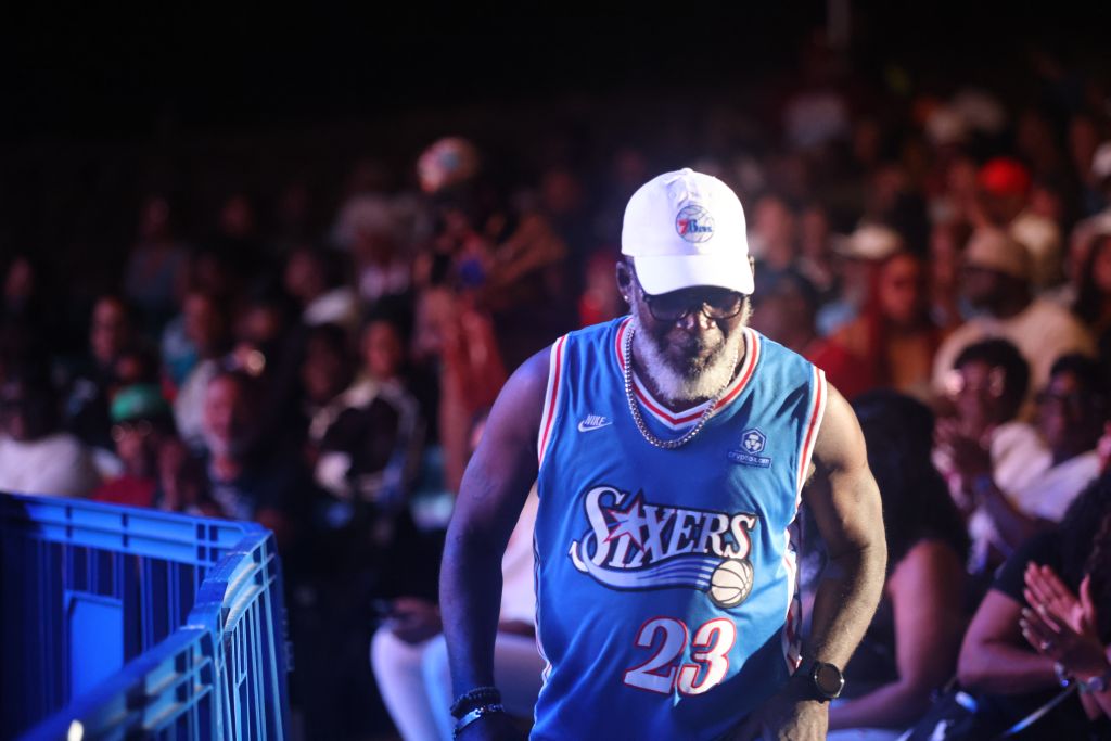 A man wearing a Philadelphia 76ers jersey with the number 23 stands in front of a cheering crowd at a basketball event.