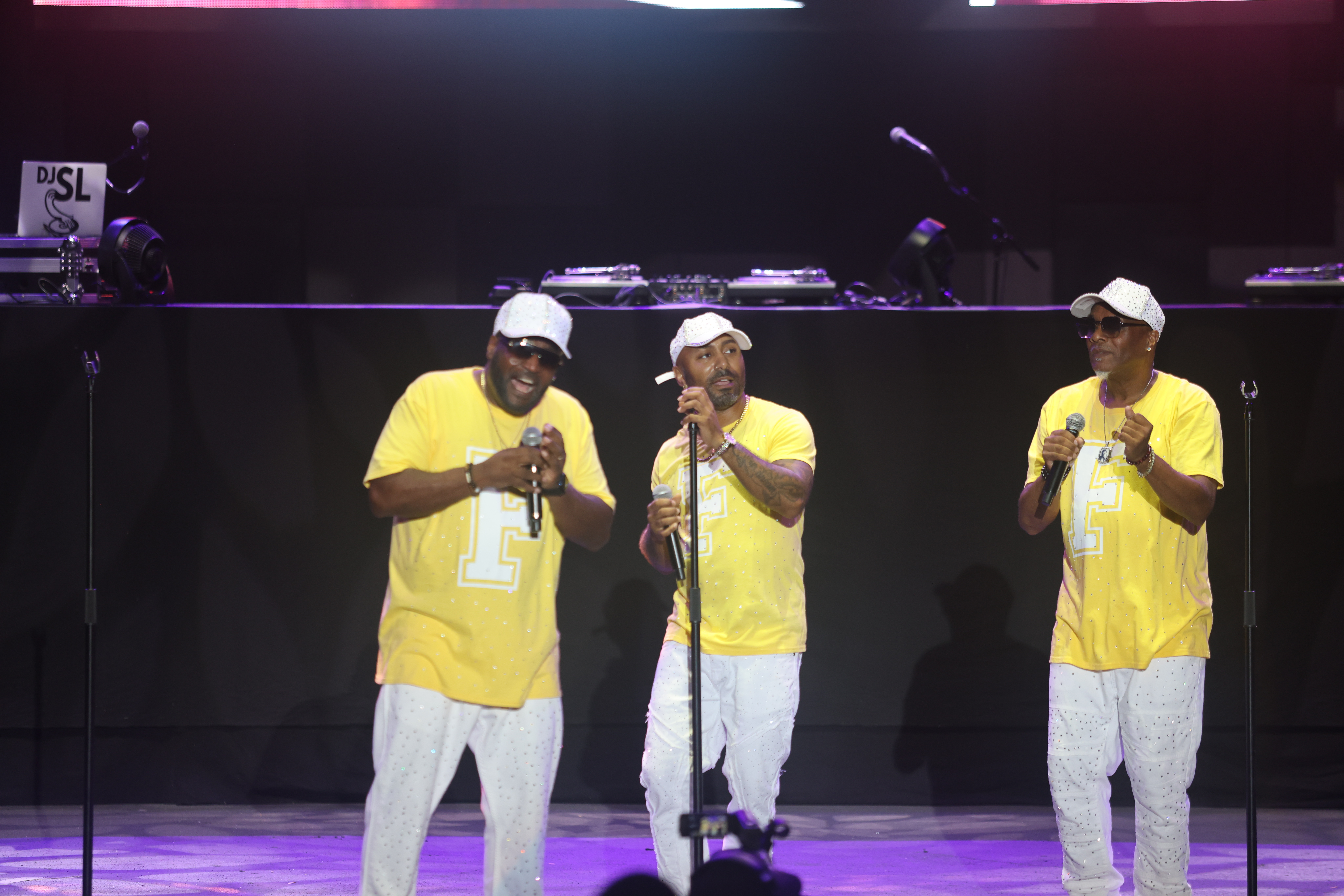 Three men in yellow shirts performing on stage with microphones.