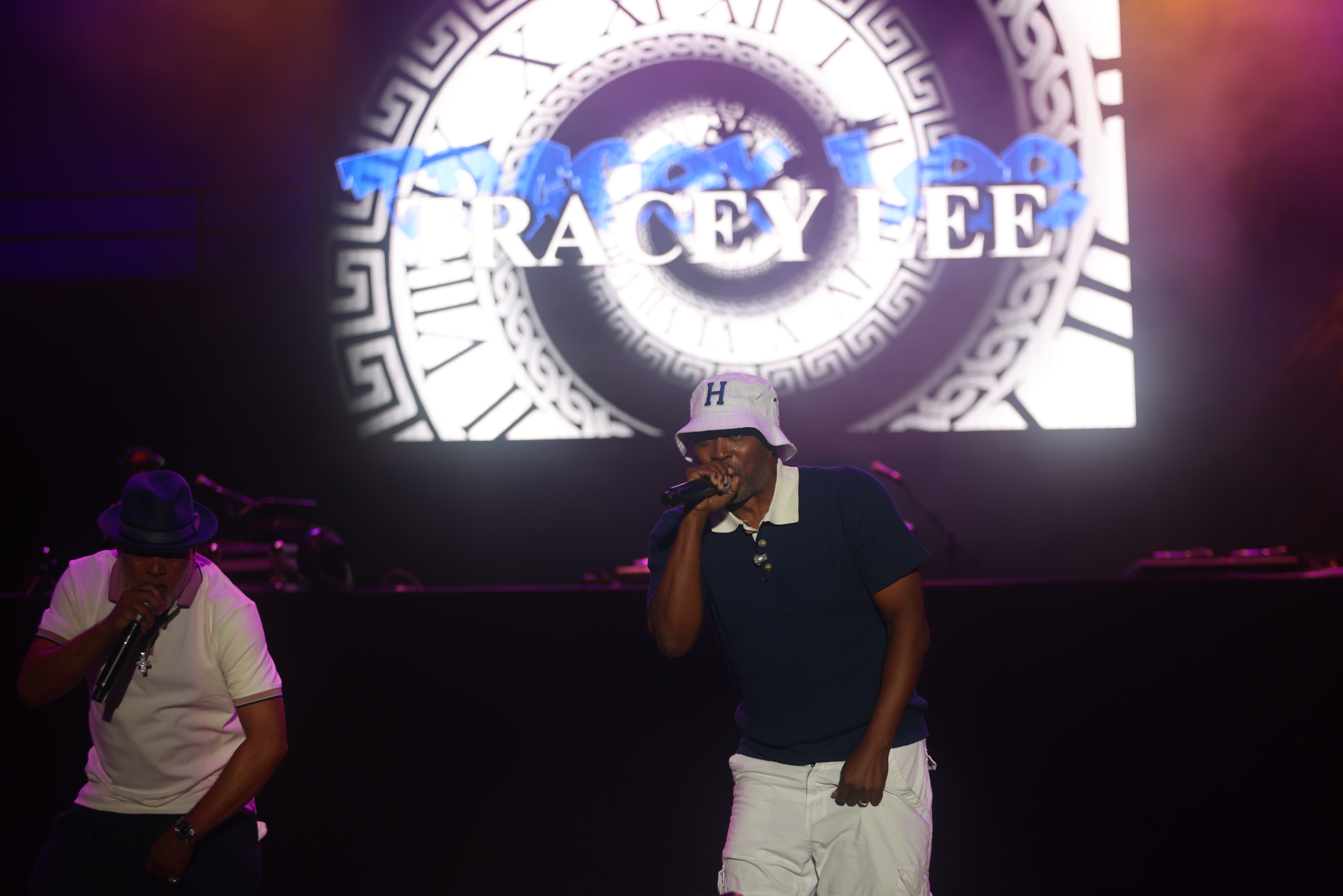 Two performers on stage in front of a large "TRACEY LEE" logo projection.