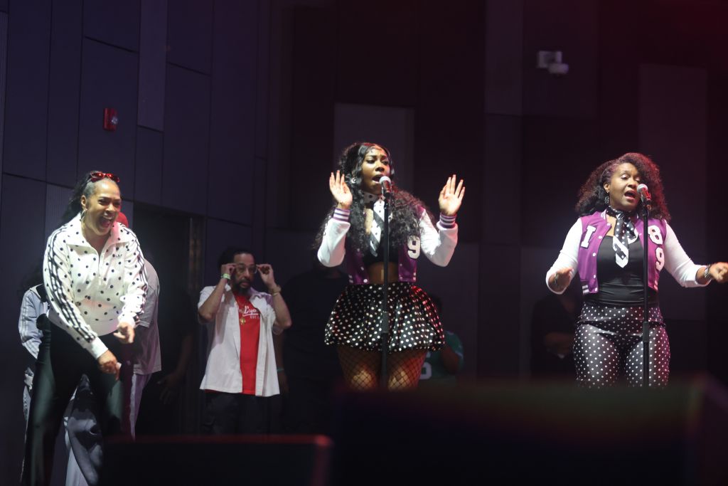 Three performers on stage singing and dancing, wearing polka dot outfits.