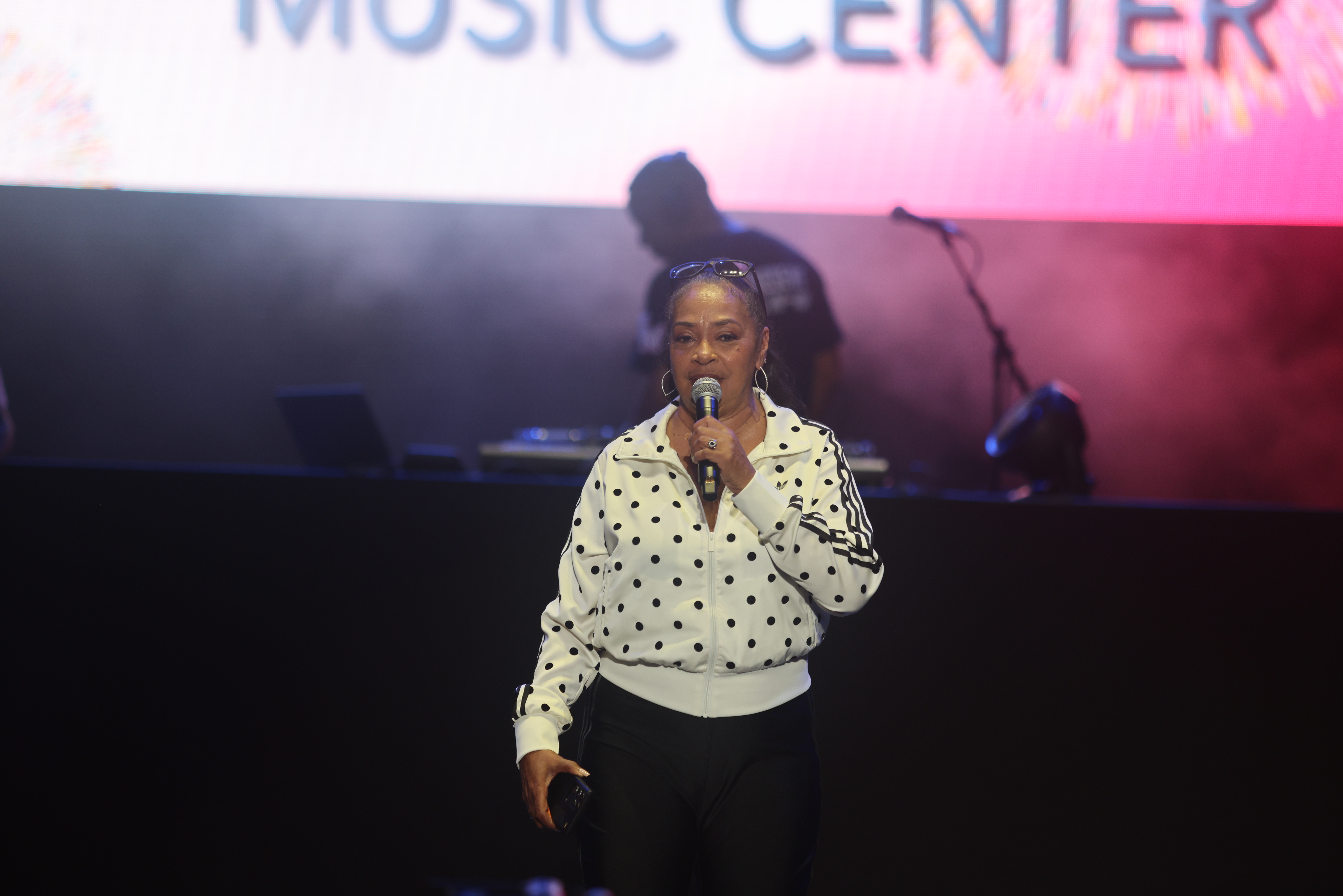 A woman in a polka dot blouse performing on stage in front of a "Music Center" backdrop.