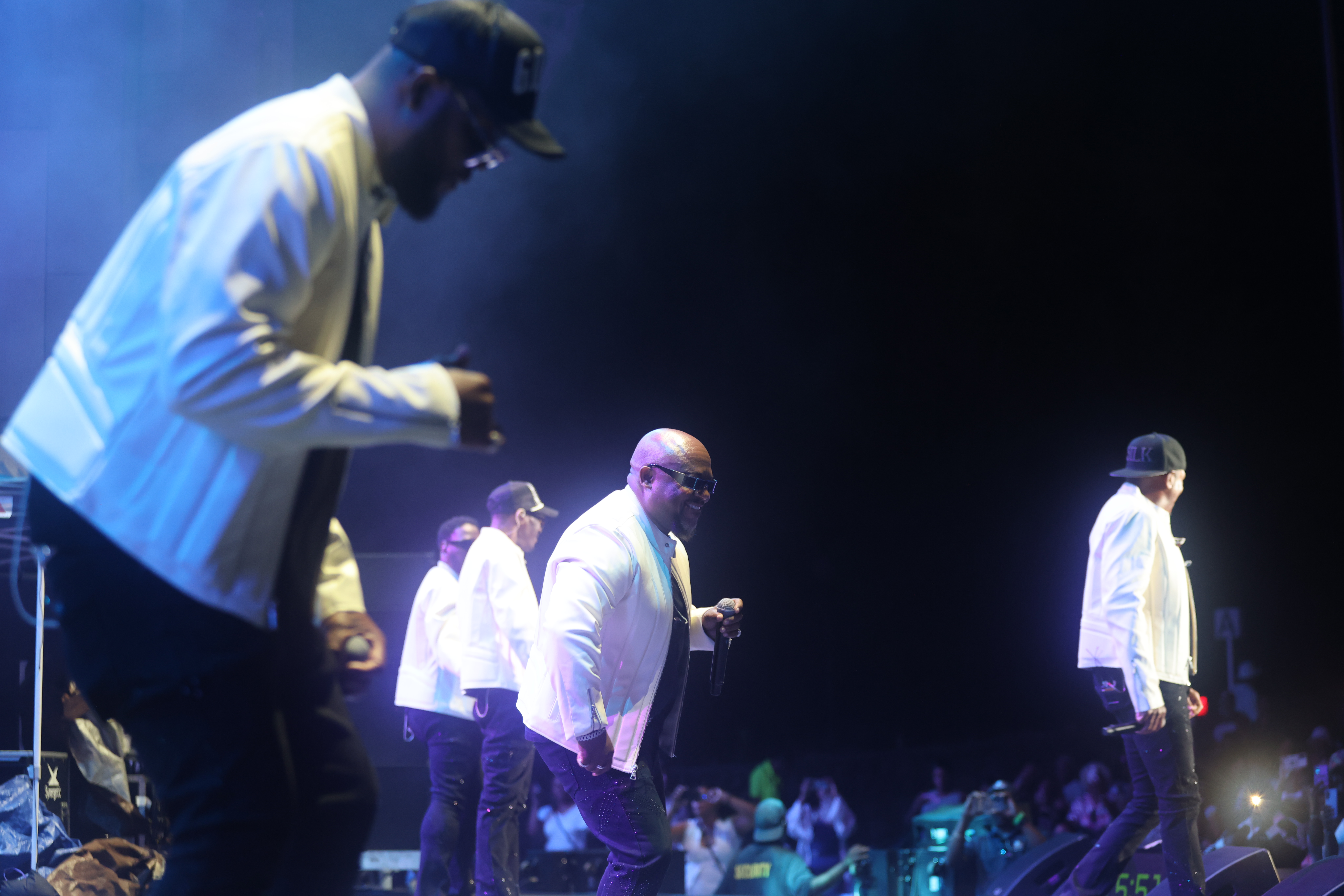 A group of performers on stage in a dimly lit venue, with one person in the foreground playing an instrument.